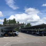 汽车停在停车场在开放式的结构(汽车港口),屋顶覆盖着太阳能电池板。天空是明亮的,毛茸茸的大云。